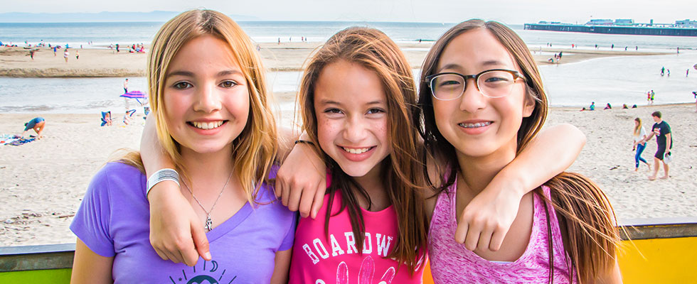 Three girls smiling in front of beach